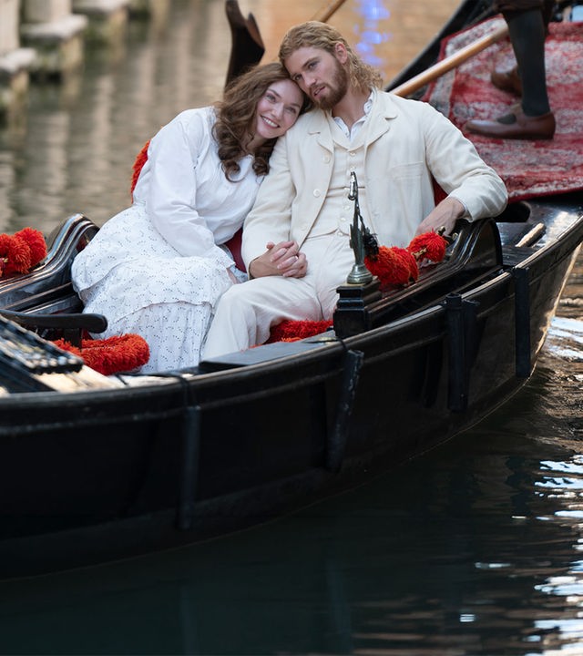 "The Forsytes - Familie verpflichtet: Heimliche Begierden": In einem Kanal in Venedig in einer Gondel: Luisa (Eleanor Tomlinson) lehnt ihren Kopf an Joylons (Danny Griffin) Schulter, beide sind weiß gekleidet. Hinter ihnen steht der Gondolière, der bis zur Hüfte zu erkennen ist.
