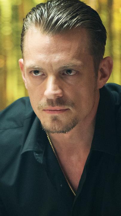 Pete Koslow (Joel Kinnaman) sitzt auf einem Stuhl und schaut eine Person an, die lediglich von hinten zu sehen ist.