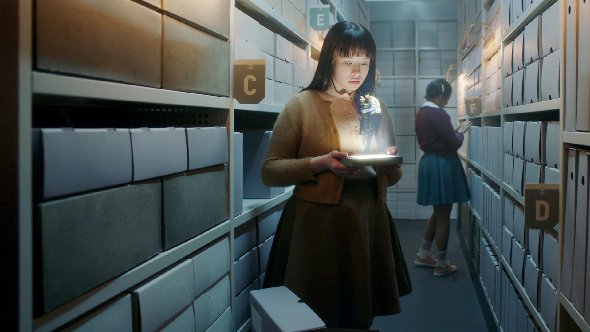 "The Ordinaries": Paula (Fine Sendel) steht im Gang eines Archivs und schaut auf ein Hologramm, welches sie in ihren Händen hält.  