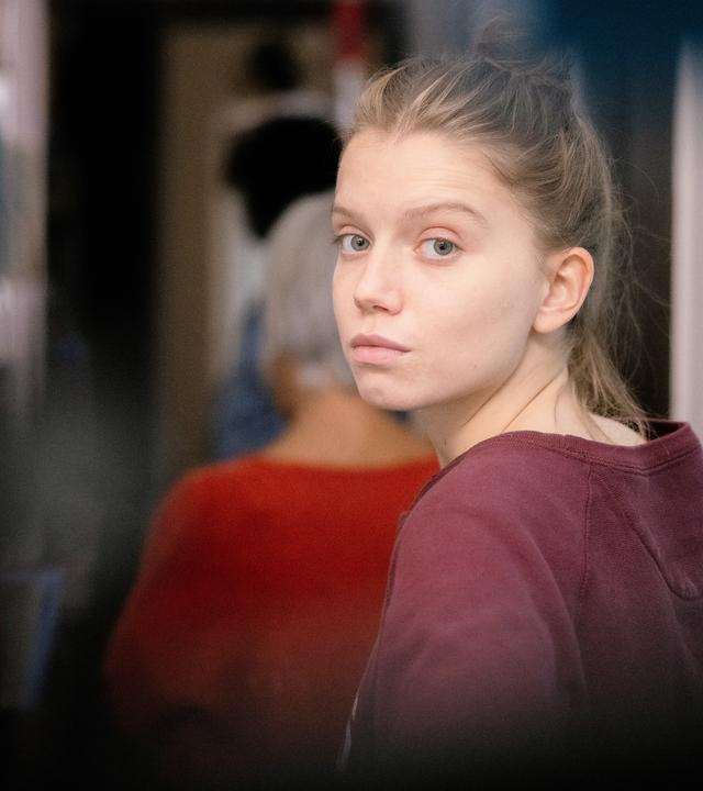 "The Perfect Mother (3)": Nahaufnahme. Anya (Eden Ducourant) läuft in einer Wohnung in einen Flur. Sie schaut sich um und blickt verzweifelt direkt in die Kamera. Vor ihr läuft, unscharf zu erkennen, ihre Großmutter Élisabeth (Frédérique Tirmont).