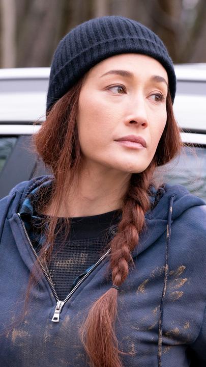Anna (Maggie Q) steht im Trainingsanzug vor einem Auto.
