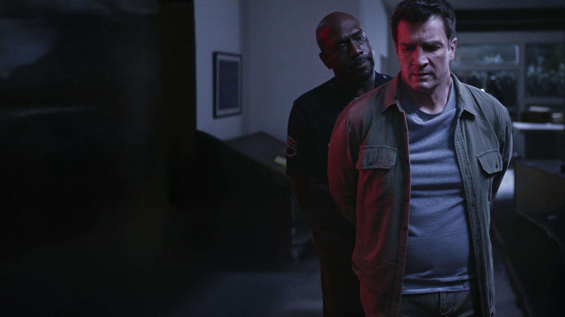 "The Rookie - Abwärts": Nolan (Nathan Fillion) steht mit den Armen hinter seinem Rücken vor Sergeant Grey (Richard T. Jones), der Nolan Handschellen umlegt und ihn dabei ernst anschaut.