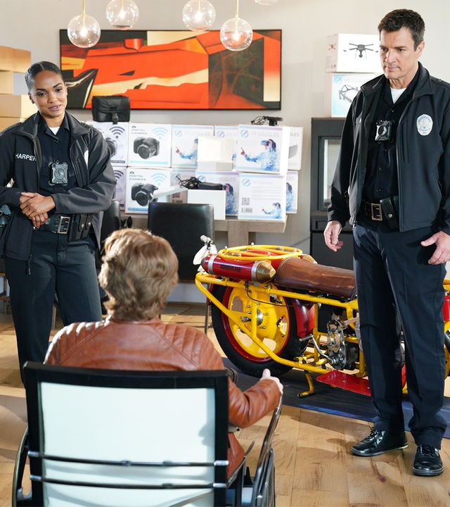 "The Rookie - Hand ab”: John Nolan (Nathan Fillion) und Nyla Harper (Mekia Cox) stellen den Identitätsdieb in seinem Wohnzimmer zwischen Kartons mit Kameras und Drohnen, sowie einem Motorrad.
