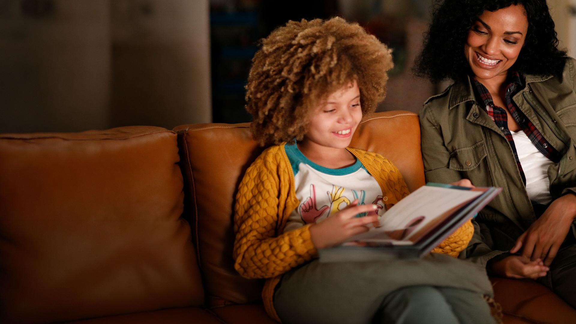 "The Rookie - Nachts": Nyla Harper (Mekia Cox) sitzt mit ihrer Tochter Lila (Carsyn Rose) auf der Couch und liest in einem Buch.