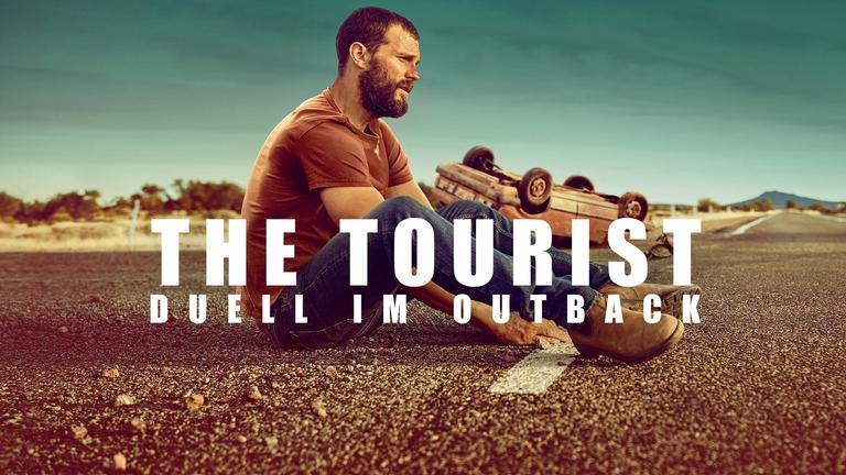 The Tourist (Sendungsteaser): Der Mann (Jamie Dornan) sitzt auf der Straße. Im Hintergrund liegt sein verunglücktes Auto auf dem Dach.