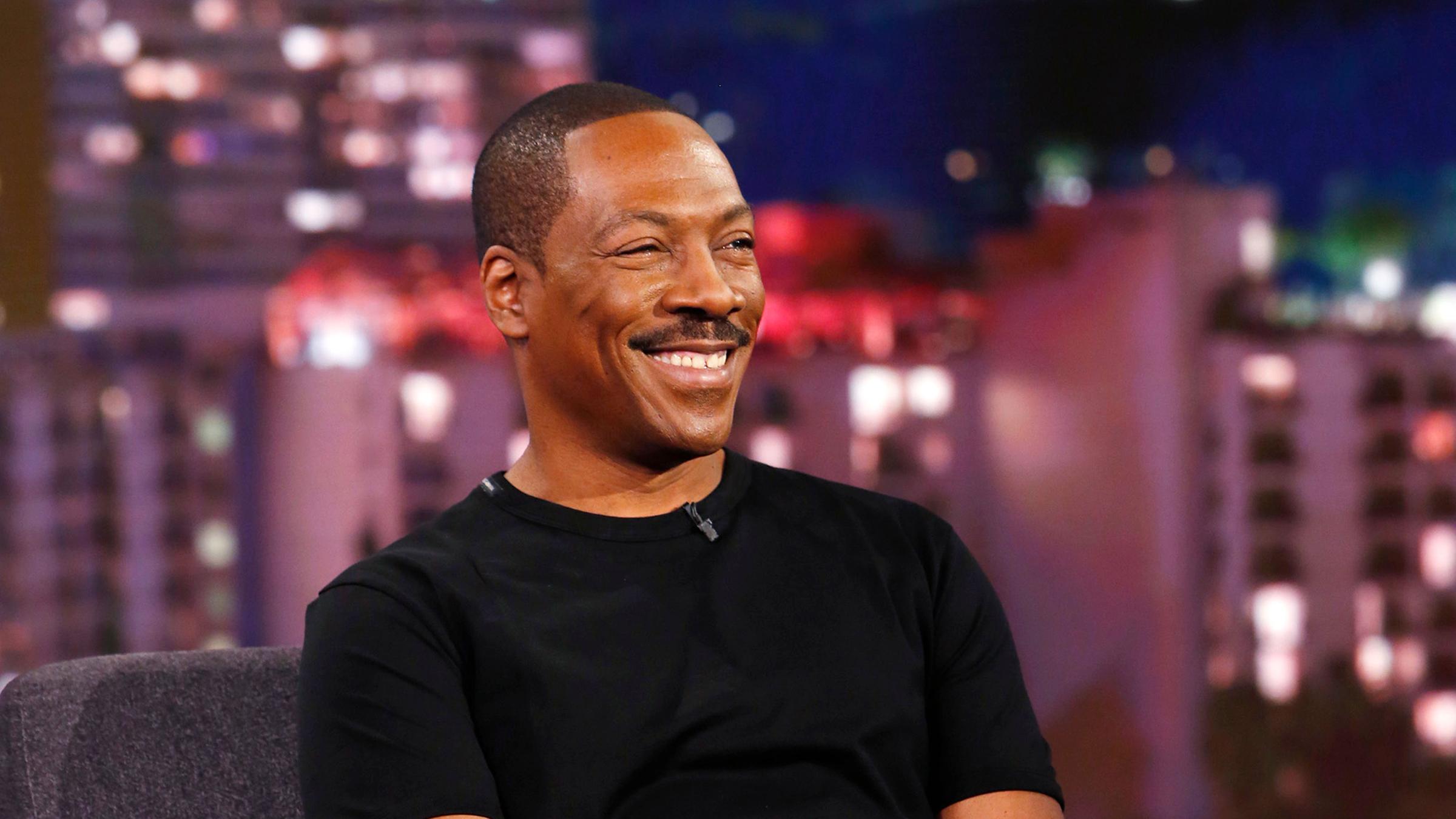 "The True Story of Eddie Murphy": Eddie Murphy sitzt schwarz gekleidet auf einem Sessel in einer Show und lacht.