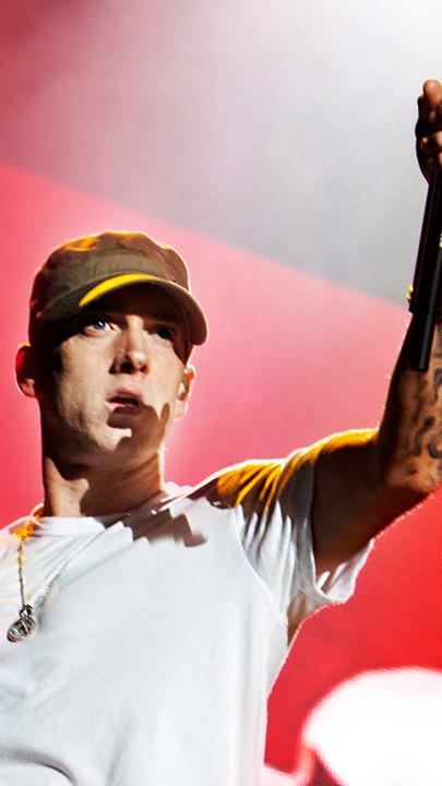 Eminem in einem weißen T-shirt vor einem roten Hintergrund.