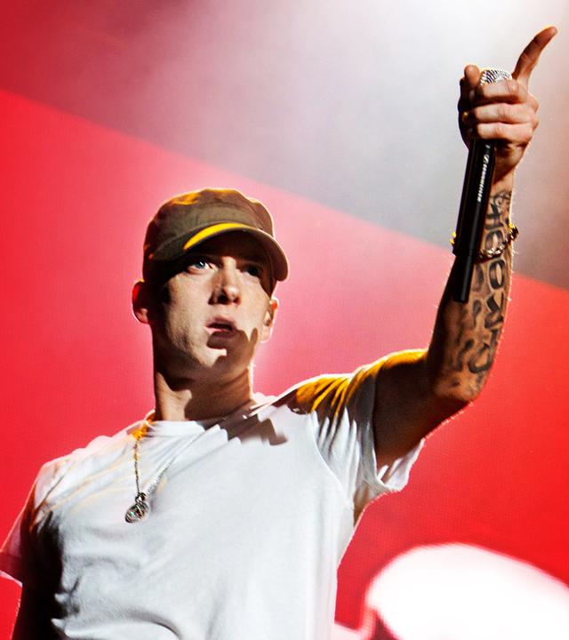 Eminem in einem weißen T-shirt vor einem roten Hintergrund.