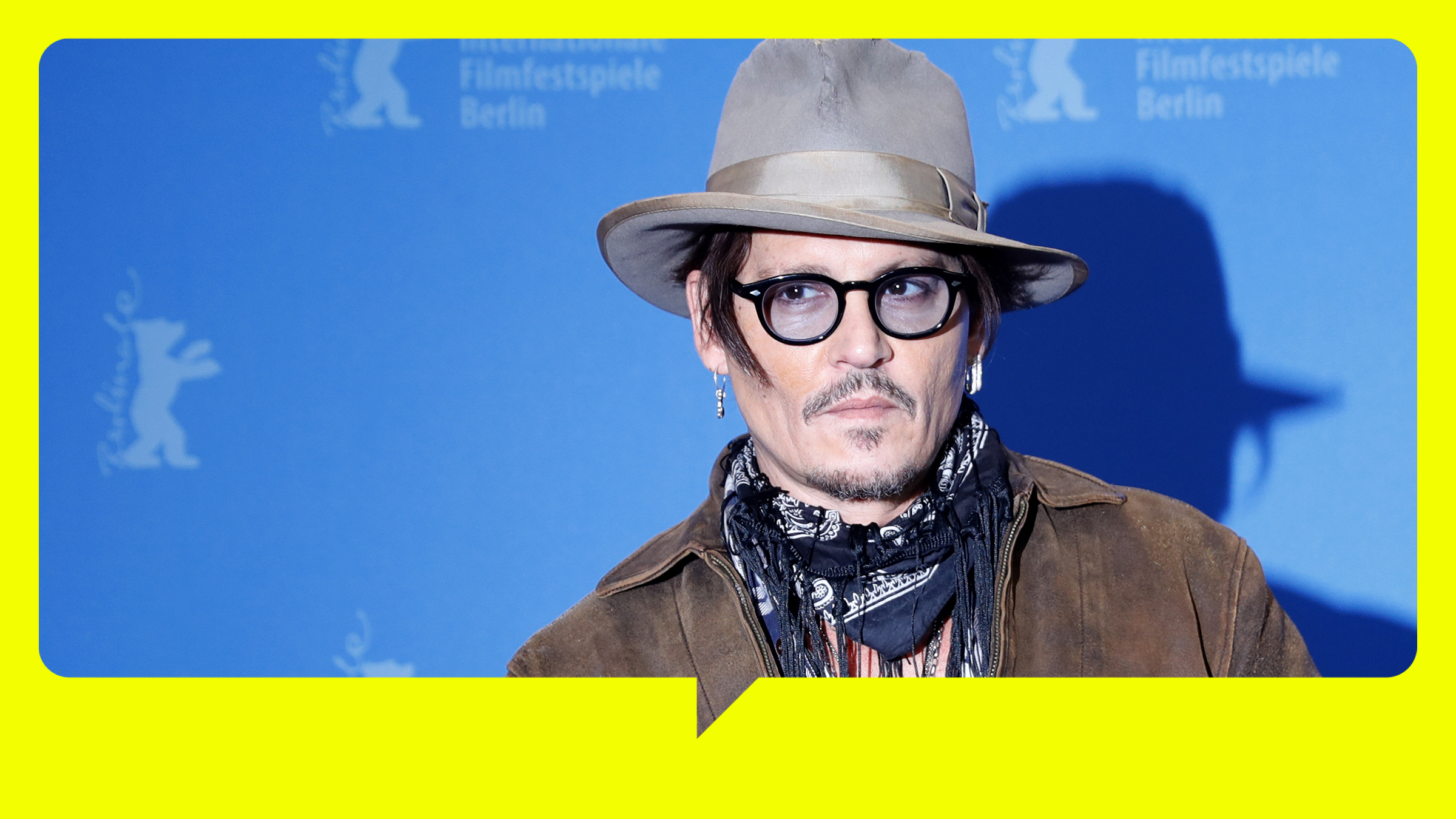 Johnny Depp steht, mit Hut und schwarzer Brille, vor einer blauen Wand.