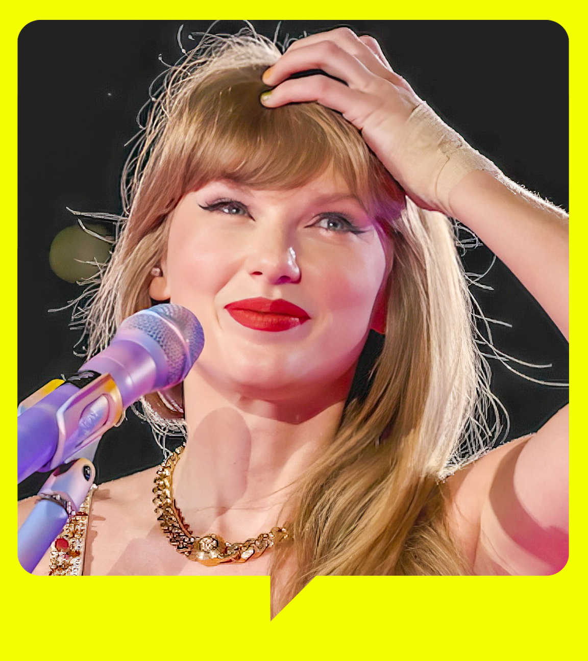 Taylor Swift steht mit Gitarre an einem Mikrofon. Sie lächelt und fasst sich an den Kopf.