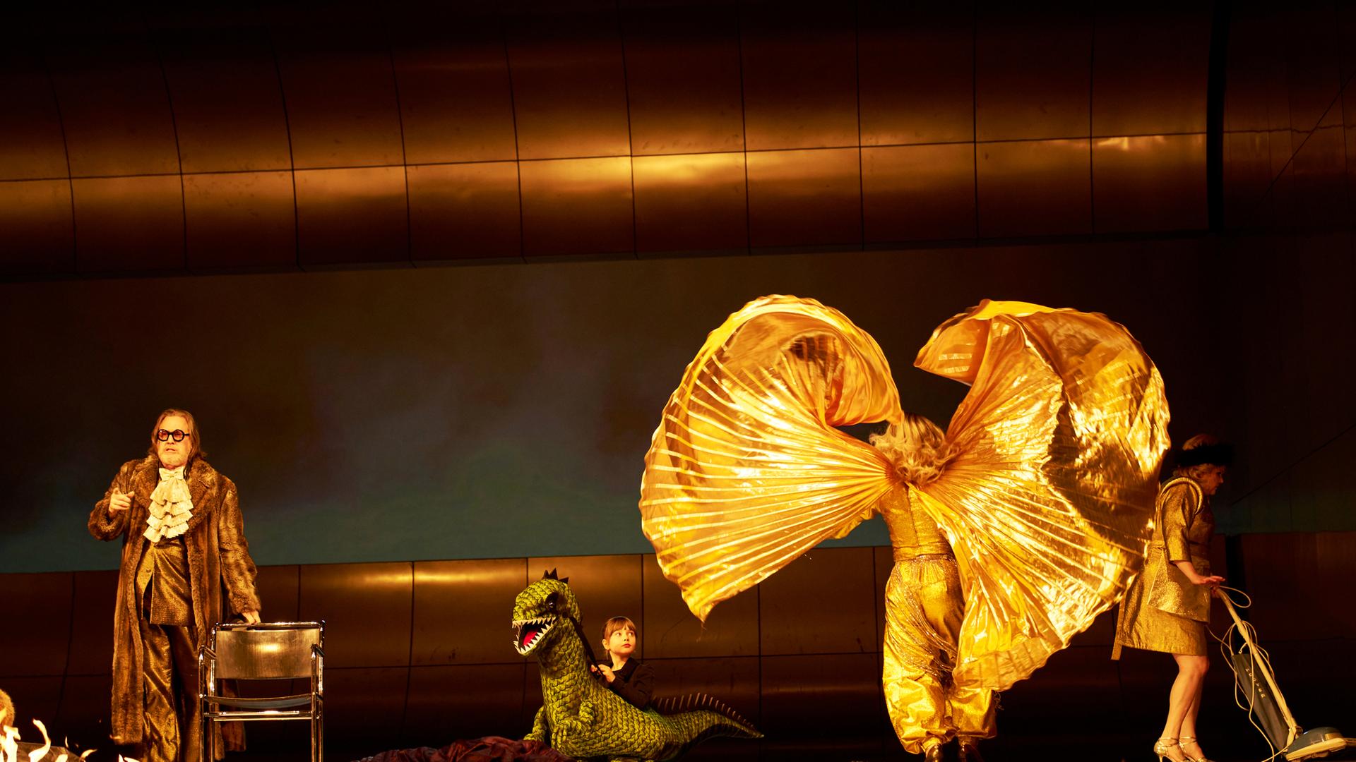 4 Schauspieler*innen auf einer Bühne. Eine wirbelt einen goldenen Mantel in die Luft.