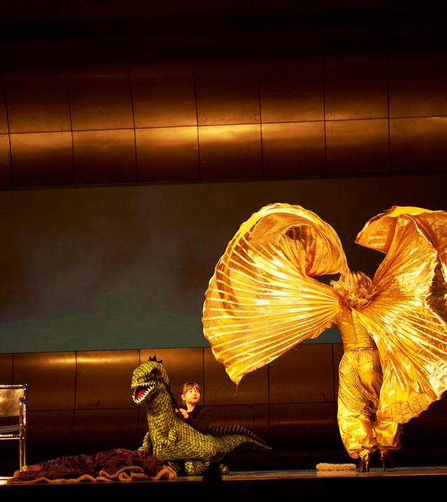 4 Schauspieler*innen auf einer Bühne. Eine wirbelt einen goldenen Mantel in die Luft.