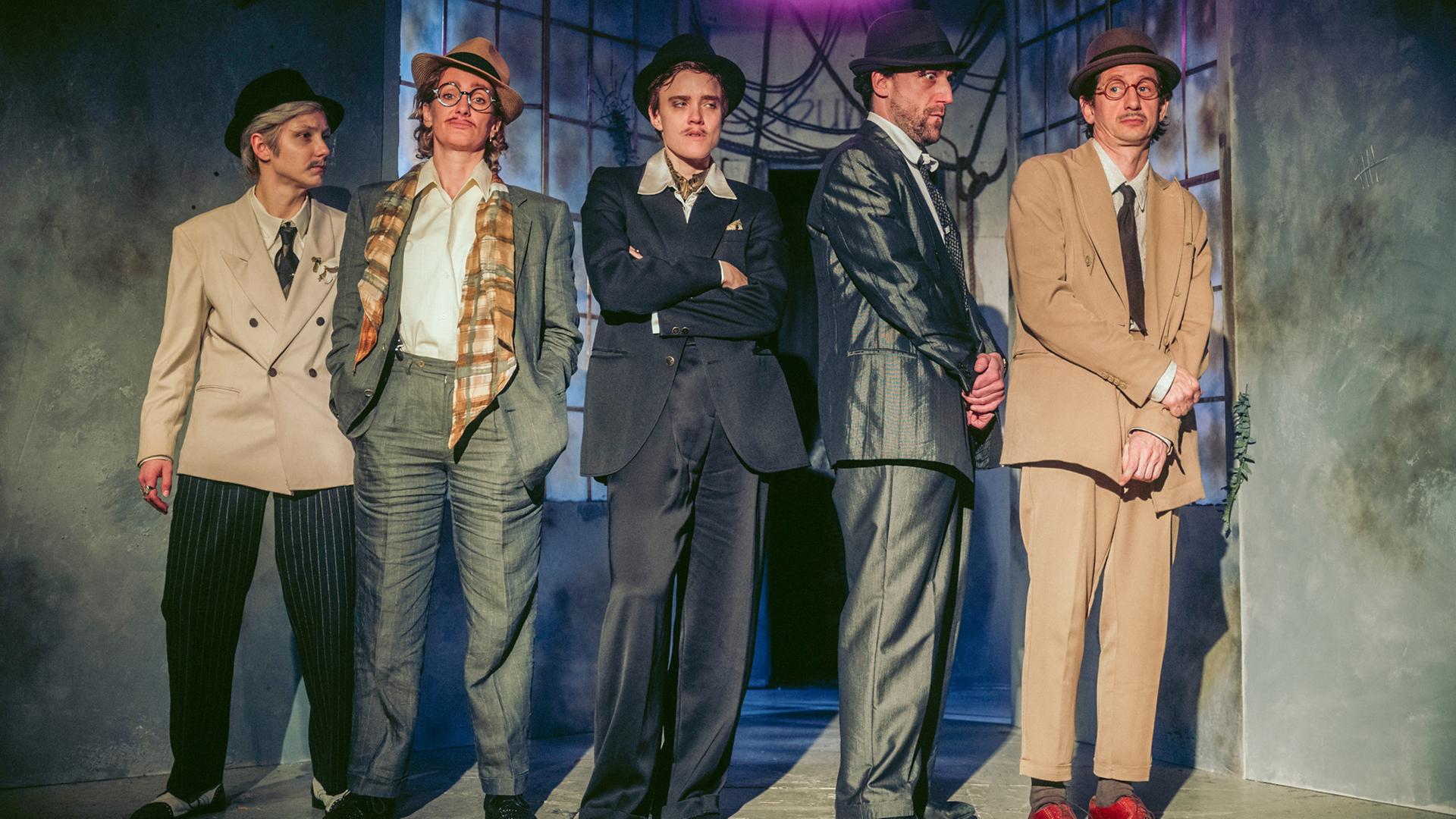 Fünf Personen mit Anzügen und Hüten bekleidet stehen auf der Bühne.