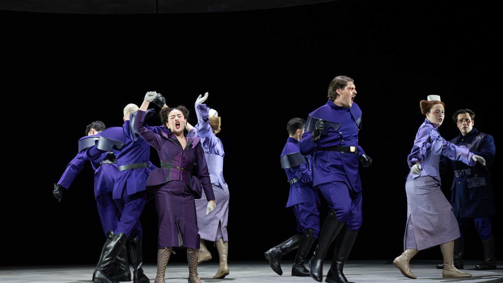 Bühnenszene: Menschen in violett-farbener Bekleidung tanzen auf einer Bühne.