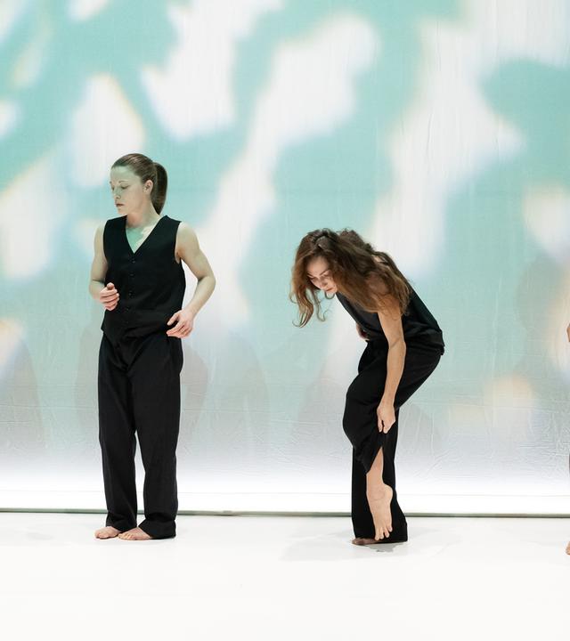 Bühnenszene: Tänzerinnen und Tänzer die schwarzeTrikots tragen, tanzen auf der Bühne.