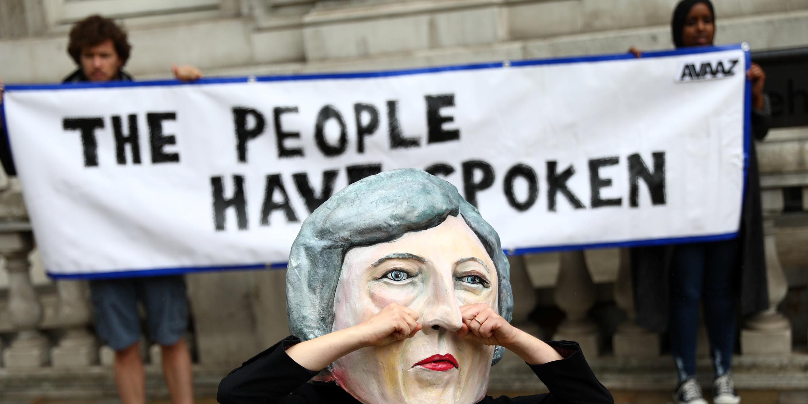 Demonstranten tragen eine Theresa May Maske, die weint.