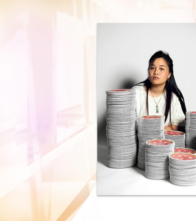 Fotografie einer asiatischen Frau mit langen Haaren, die hinter mehreren Stapeln mit bunten Schüsseln sitzt.
