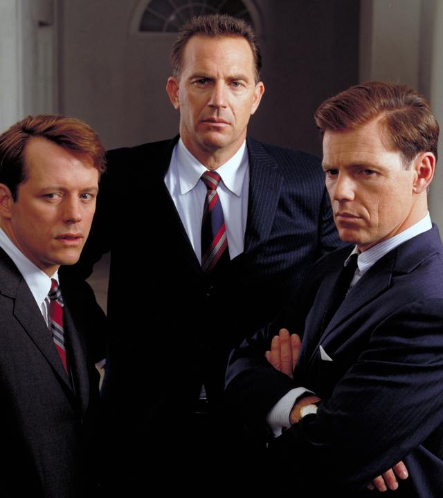 Thirteen Days: Robert Kennedy (Steven Culp, links), US-Präsident John F. Kennedy (Bruce Greenwood, rechts) und Präsidentenberater Kenneth ODonnell (Kevin Costner, Mitte) stehen in dunklen Anzügen nebeneinander und blicken ernst in die Kamera.