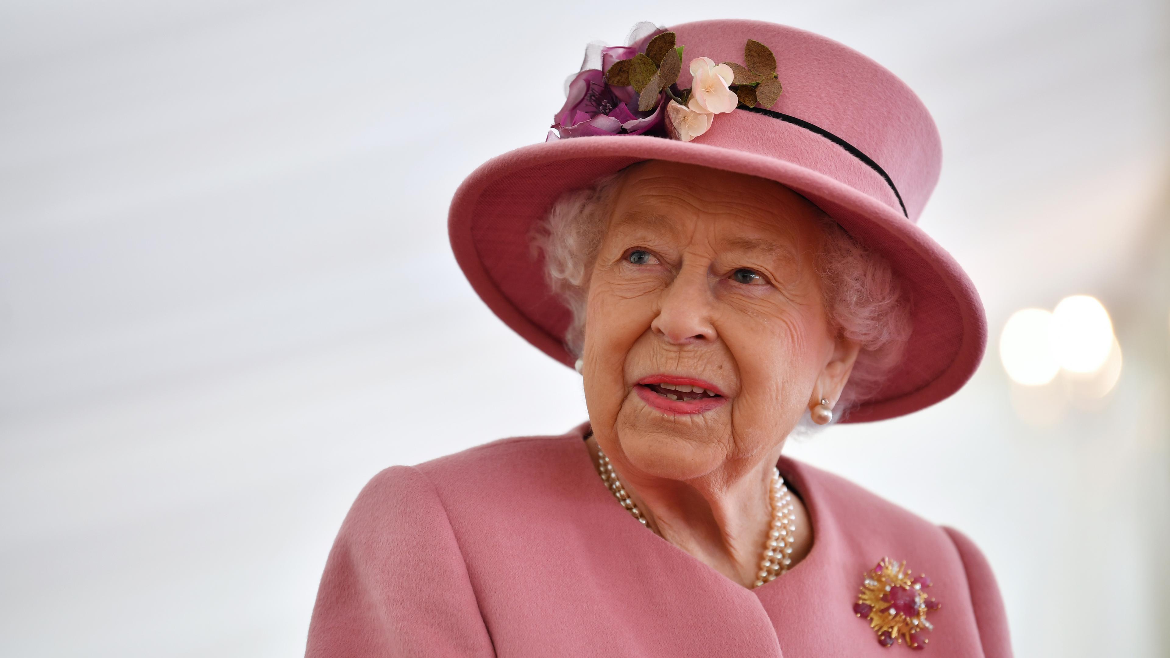 Queen Elizabeth II. blickt mit rosa Kostüm und rosa Hut zur Seite.