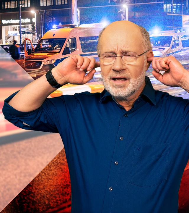 Harald Lesch hält sich die Ohren zu - auf Straße mit Einsatzfahrzeugen.