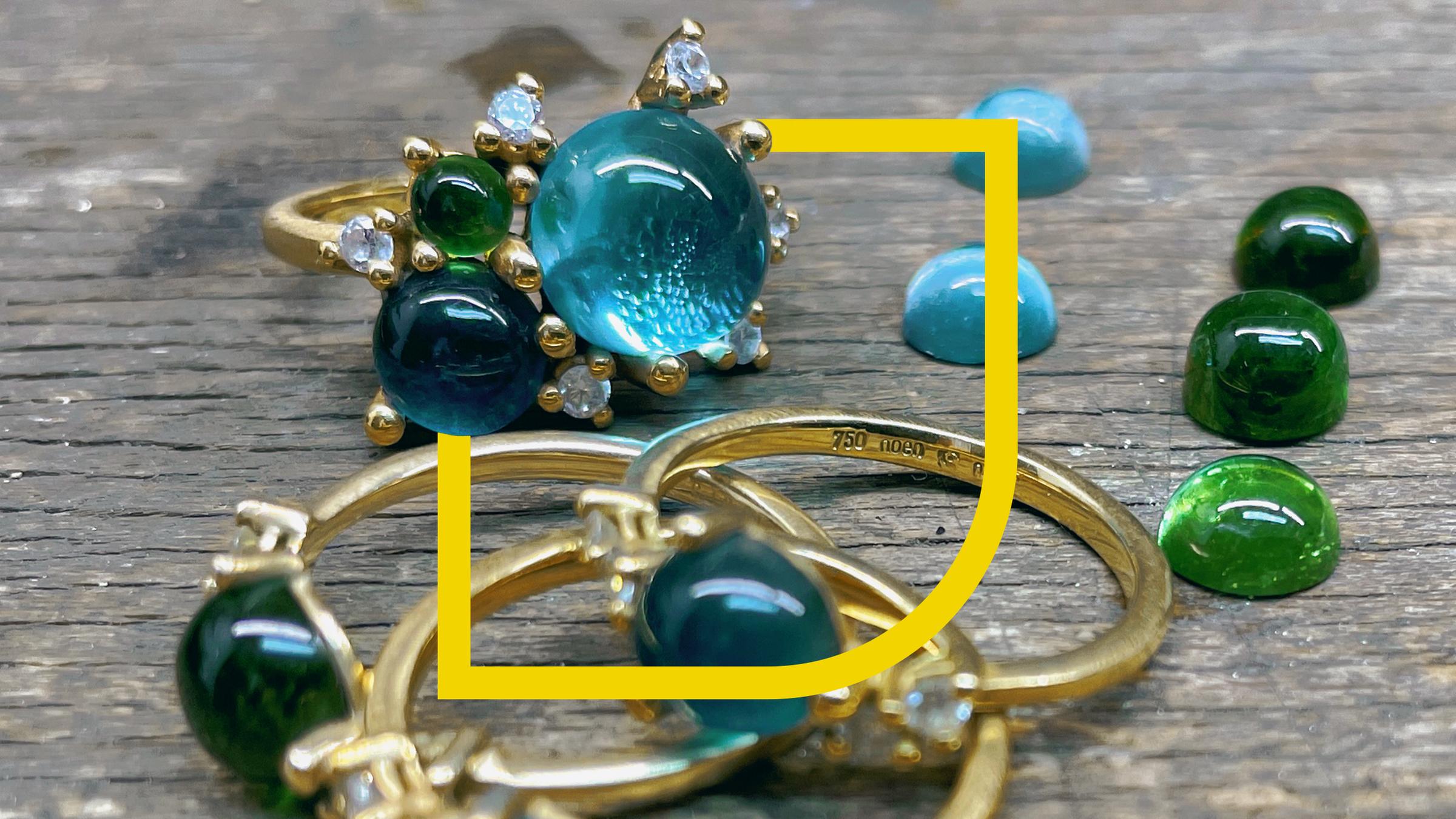 Goldene Ringe mit blau grünen Steinen verziert liegen auf einem Holztisch