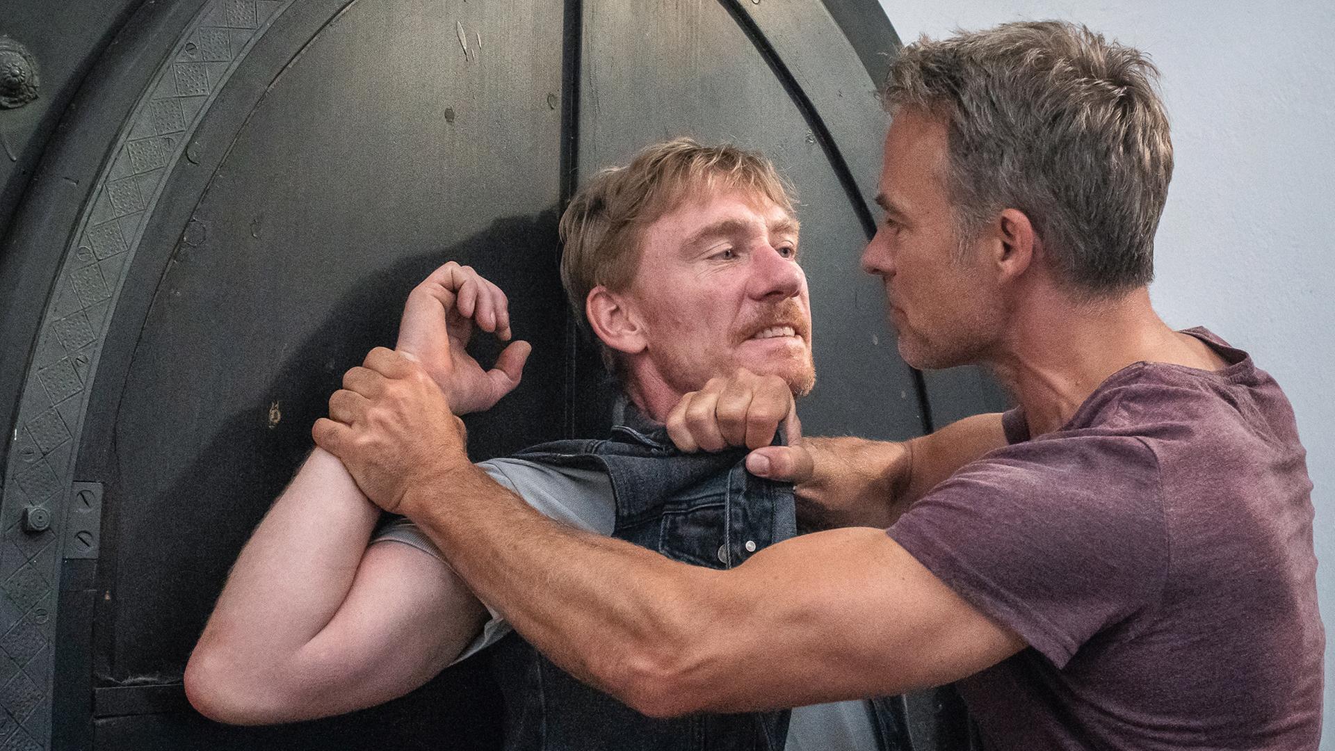 Jan Maybach hat Boris Moll am Kragen seiner Weste gepackt und drückt ihn gegen die Tür der Kirche