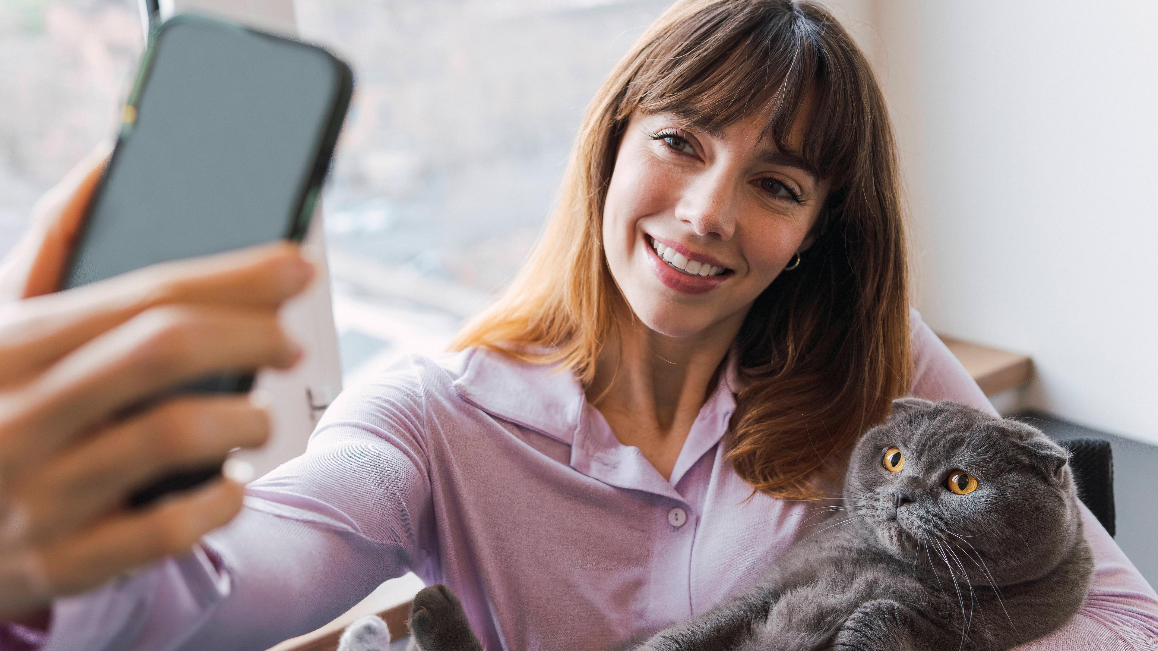 Eine Frau hält eine Katze auf dem Arm und fotografiert sich mit dem Smartphone.
