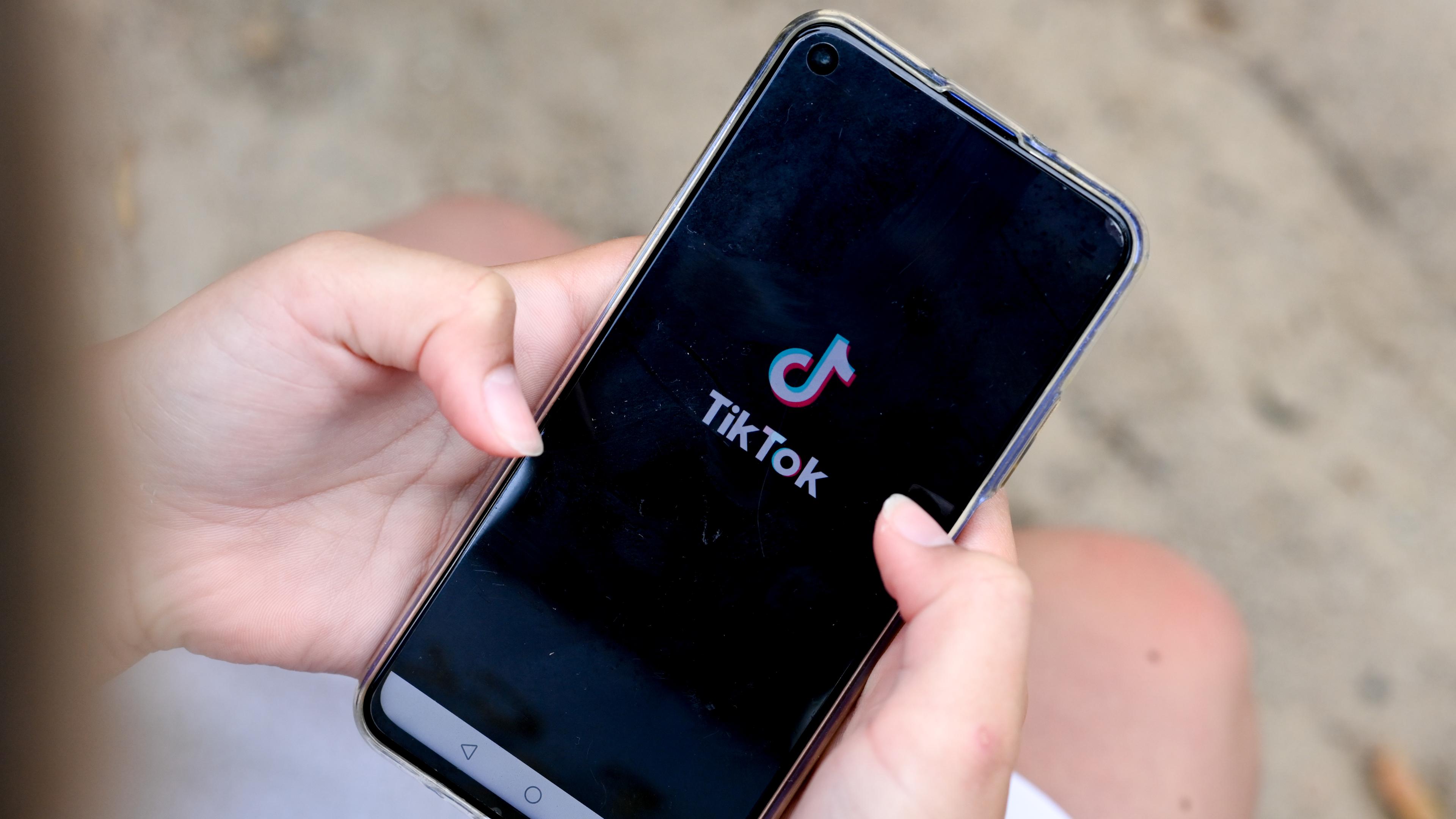 Hände halten ein Smartphone, auf dem das TikTok-Logo zu sehen ist.