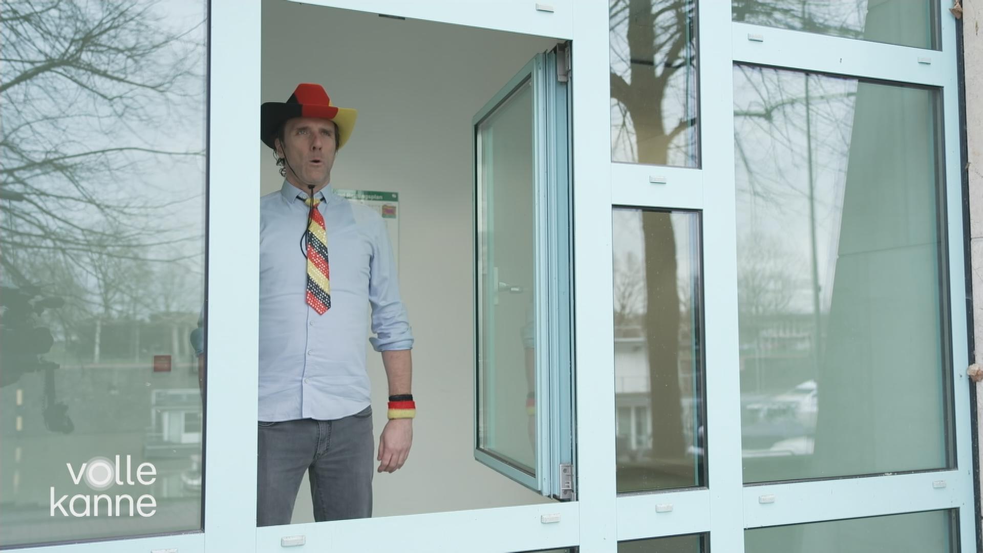 Reporter mit deutschen Accessoires (Hut, Krawatte) steht vor einem offenen Fenster.