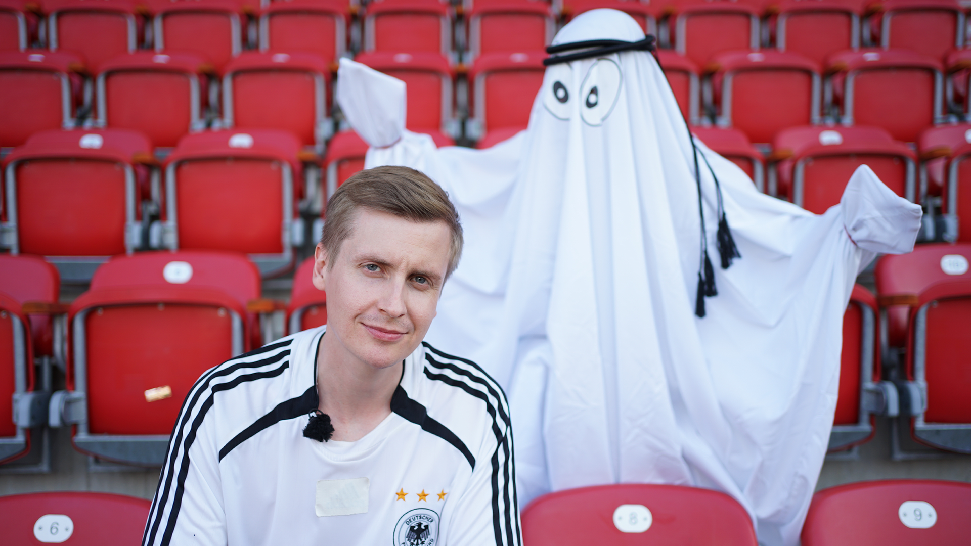 Till Reiners hat ein Fußballtrikot an und steht auf einer Fußballstribüne. Hinter ihm ist ein Gespent zu sehen.