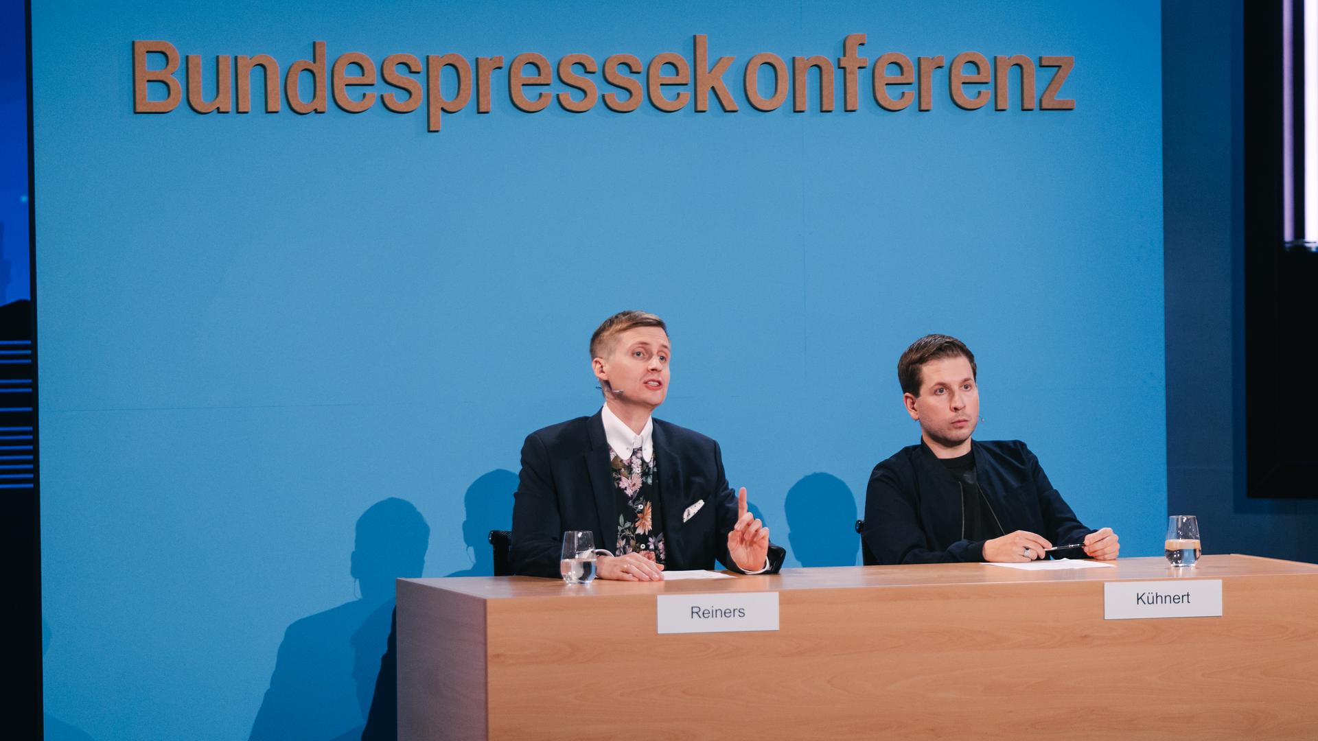 Till Reiners und Kevin Kühnert vor einer nachgebauten Wand der Bundespressekonferenz.