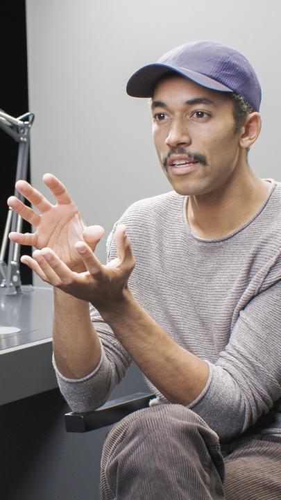 "To Show or not to Show": Benito Bause sitzt an einem Pult und gestikuliert beim Sprechen. Auf dem Bildschirm im Pult ist Sarah Blaßkiewitz zu sehen, die auch an dem Pult sitzt. Bei ihr im Bildschirm ist wiederum Angelika Levi zu sehen.