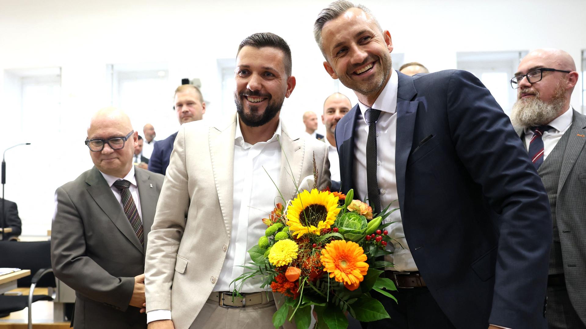 Tobias Rauch und Ulrich Siegmund lachen mit einem Blumenstrauß in der Hand