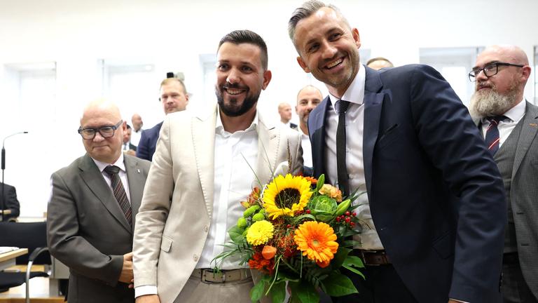 Tobias Rauch und Ulrich Siegmund lachen mit einem Blumenstrauß in der Hand