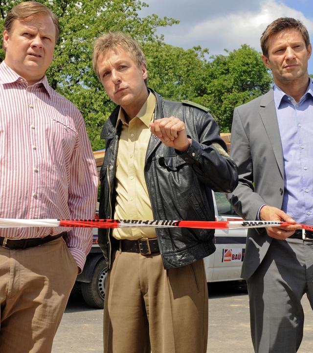 "Die Rosenheim-Cops - Tod auf der Walz": Vor einem Polizeiabsperrband stehen die Kommissare Hartl (Michael A. Grimm), Hansen (Igor Jeftic) und Polizist Mohr (Max Müller).