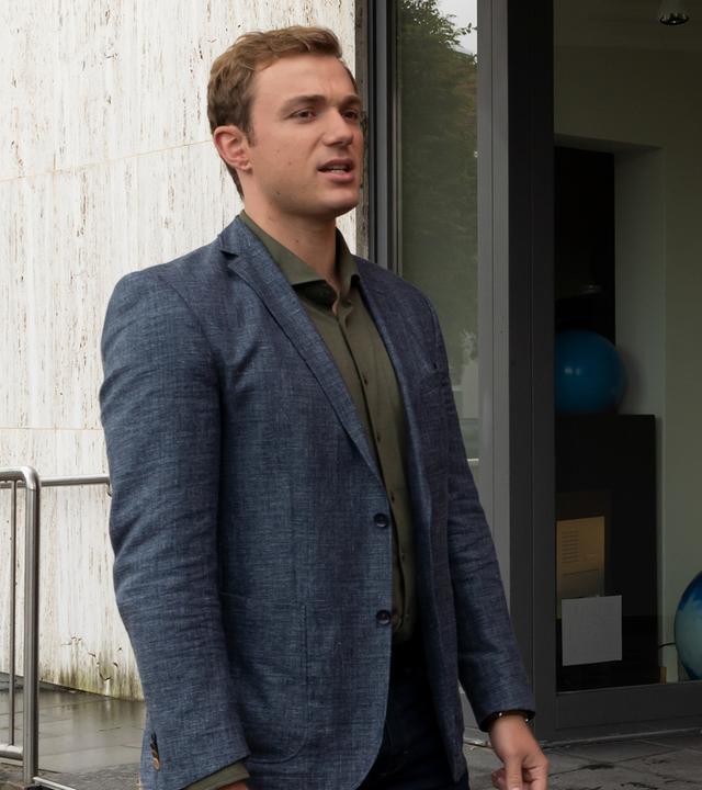 Die Kommissare Thomas (Moritz von Zeddelmann) und Laura Schmidt (Marija Kovčo) stehen am Treppenaufgang des Geschäfts "Reinsbach Elektrohandel". Auf dem Schild rechts von Laura Schmidt sind neben dem Geschäftsnamen auch die Dienstleistungen aufgeführt.