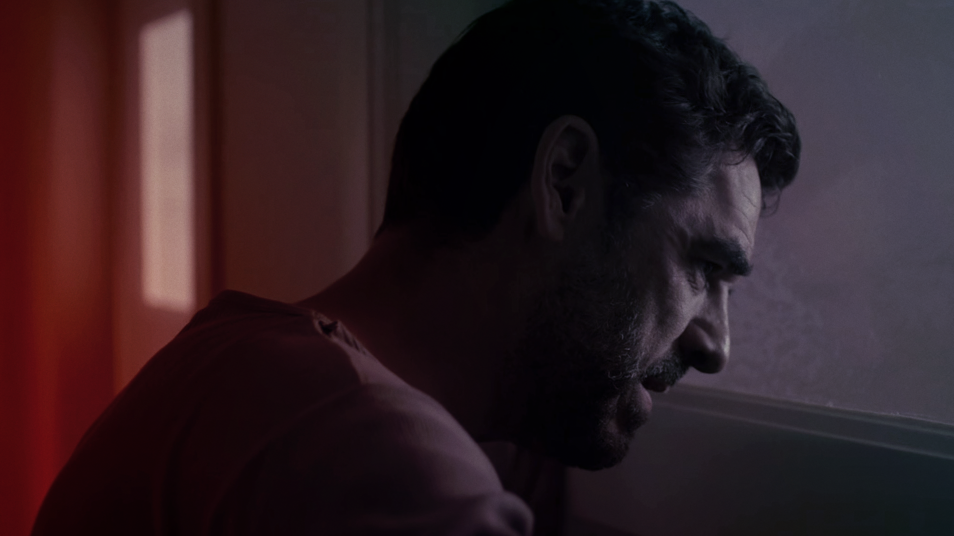 Ein Mann schaut im Halbdunkeln mit dramatisch-tragischem Blick durch das Fenster einer Kliniktür.