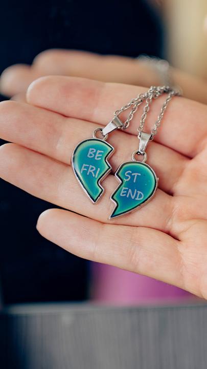 Eine Hand hält eine Kette mit zerbrochenem Herzen, dahinter steht das Foto einer jungen Frau.