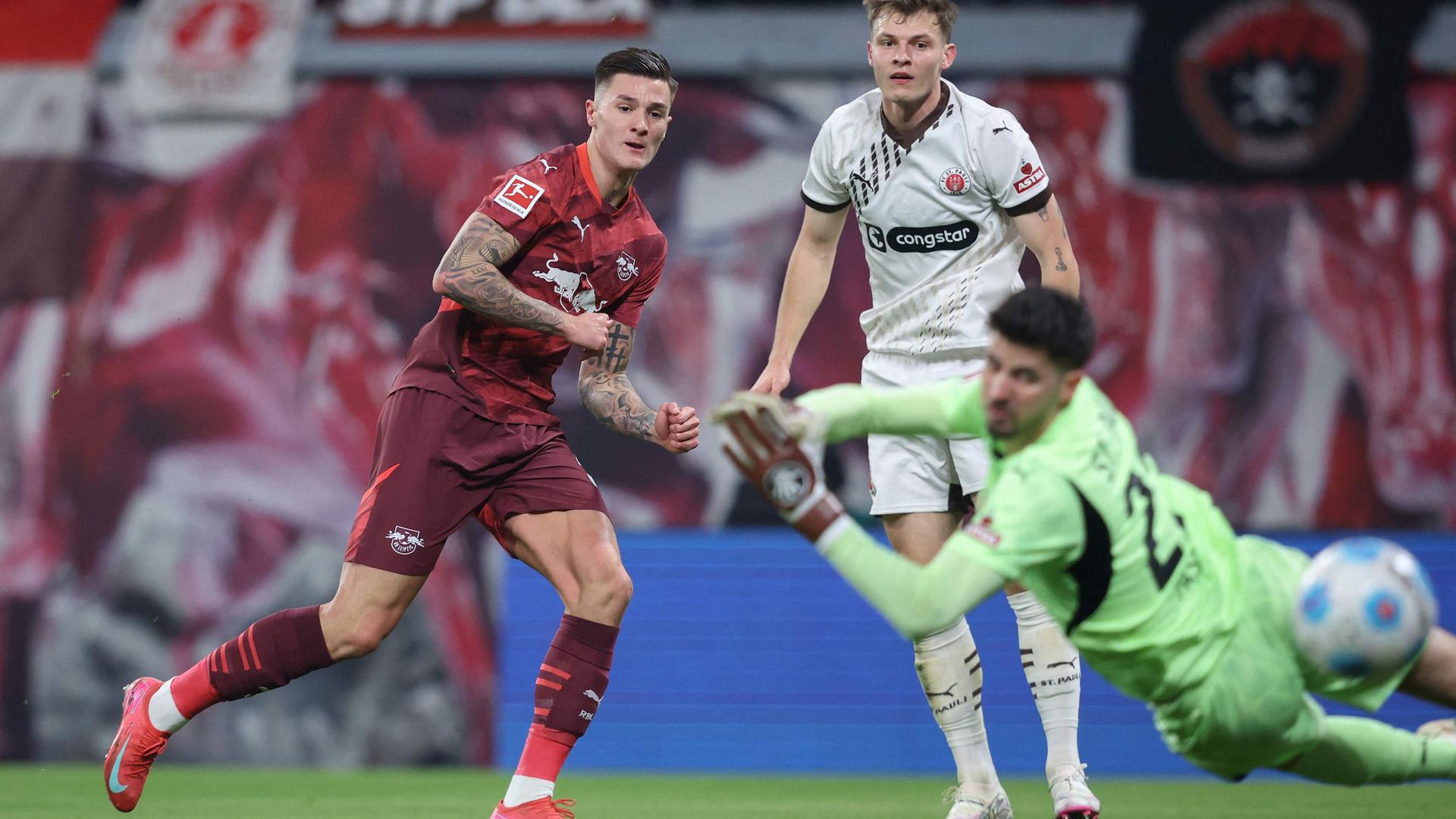 Leipzigs Stürmer (30) Benjamin Sesko (L) erzielt den Führungstreffer gegen St. Paulis Torhüter (22) Nikola Vasilj und St. Paulis Verteidiger (04) David Nemeth in Aktion.