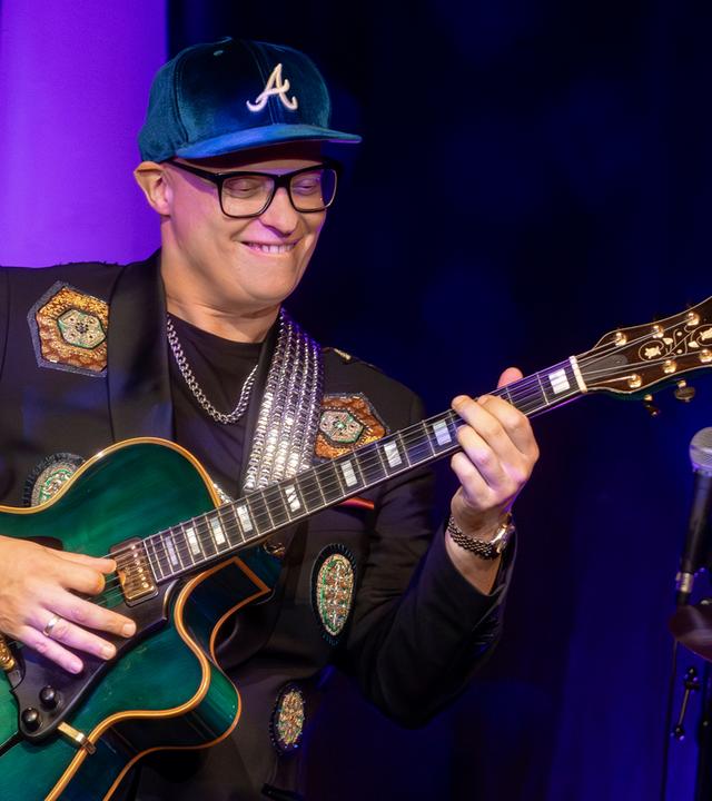 Mann steht mit Gitarre auf der Bühne