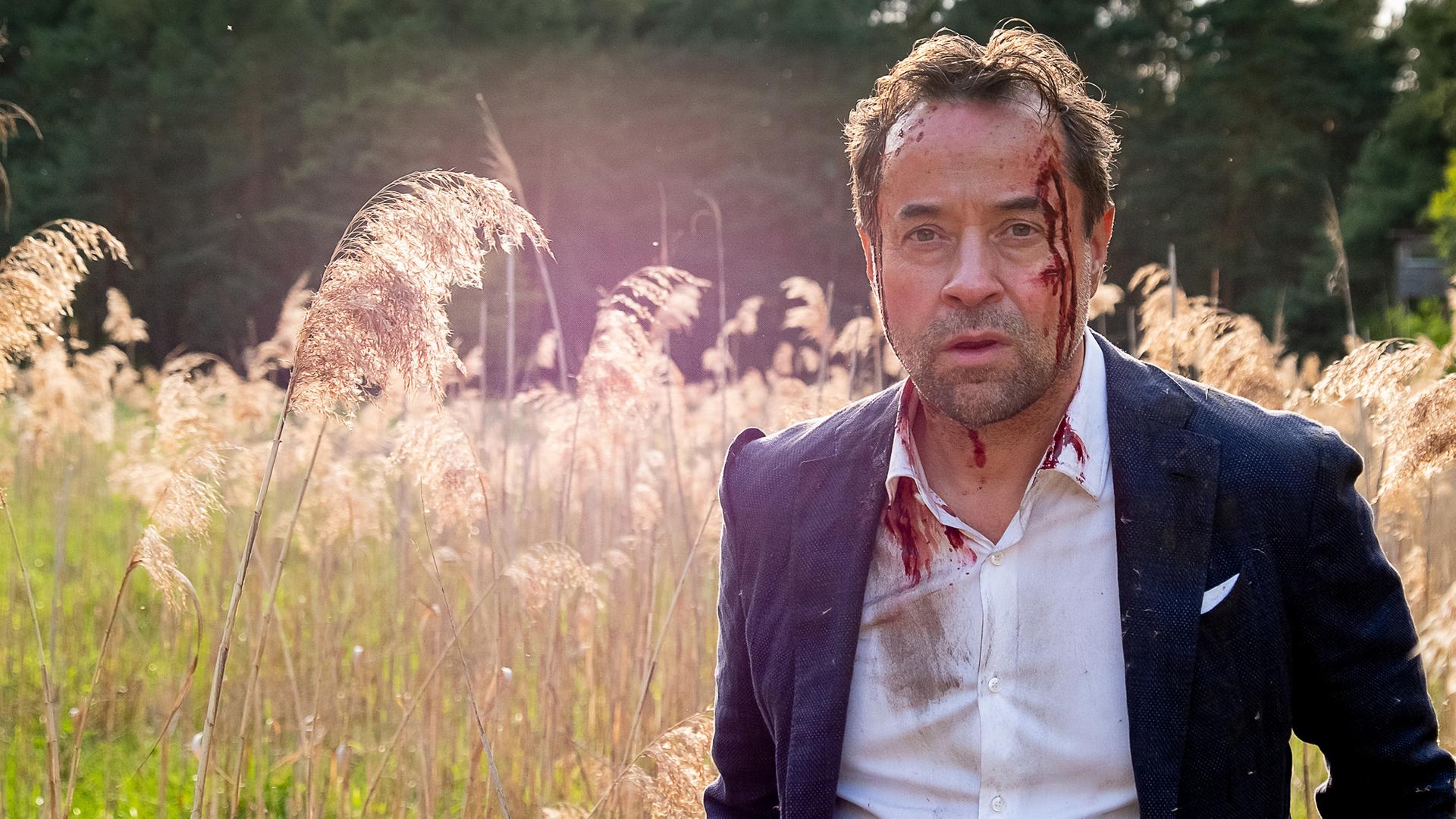 Joachim Vernau (Jan Josef Liefers) steht in einem Feld, an seiner linken Schläfe hat er eine Verletzung, die blutet.