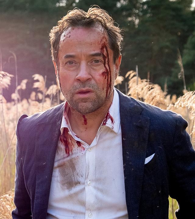 Joachim Vernau (Jan Josef Liefers) steht in einem Feld, an seiner linken Schläfe hat er eine Verletzung, die blutet.