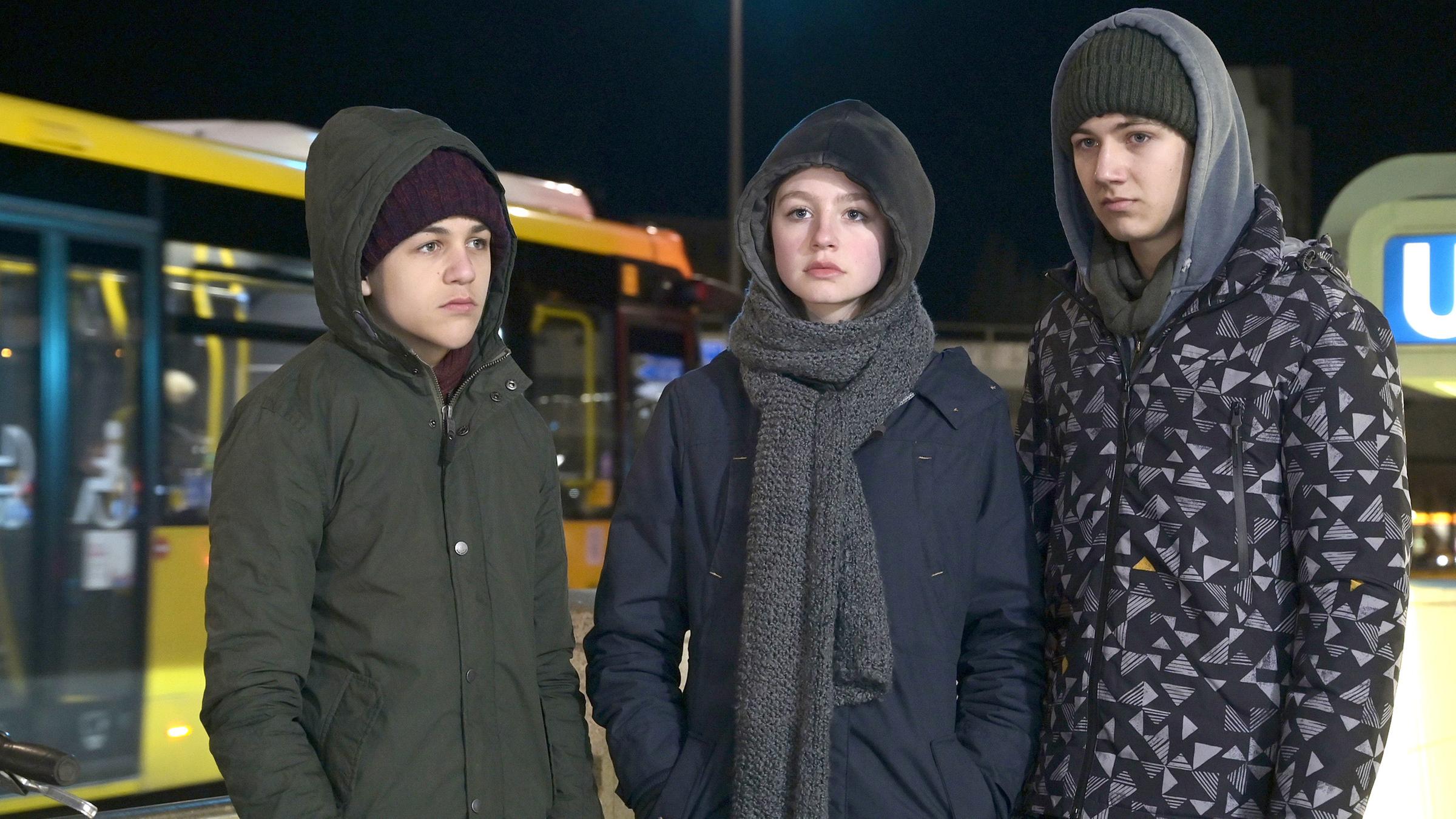 Jakob (David Ali Rashed), Mira (Flora Li Thiemann) und Fabian (Lenius Jung) stehen zusammen vor einer U-Bahnhaltestelle. Sie schauen sich nicht an, jeder starrt konsterniert vor sich hin.