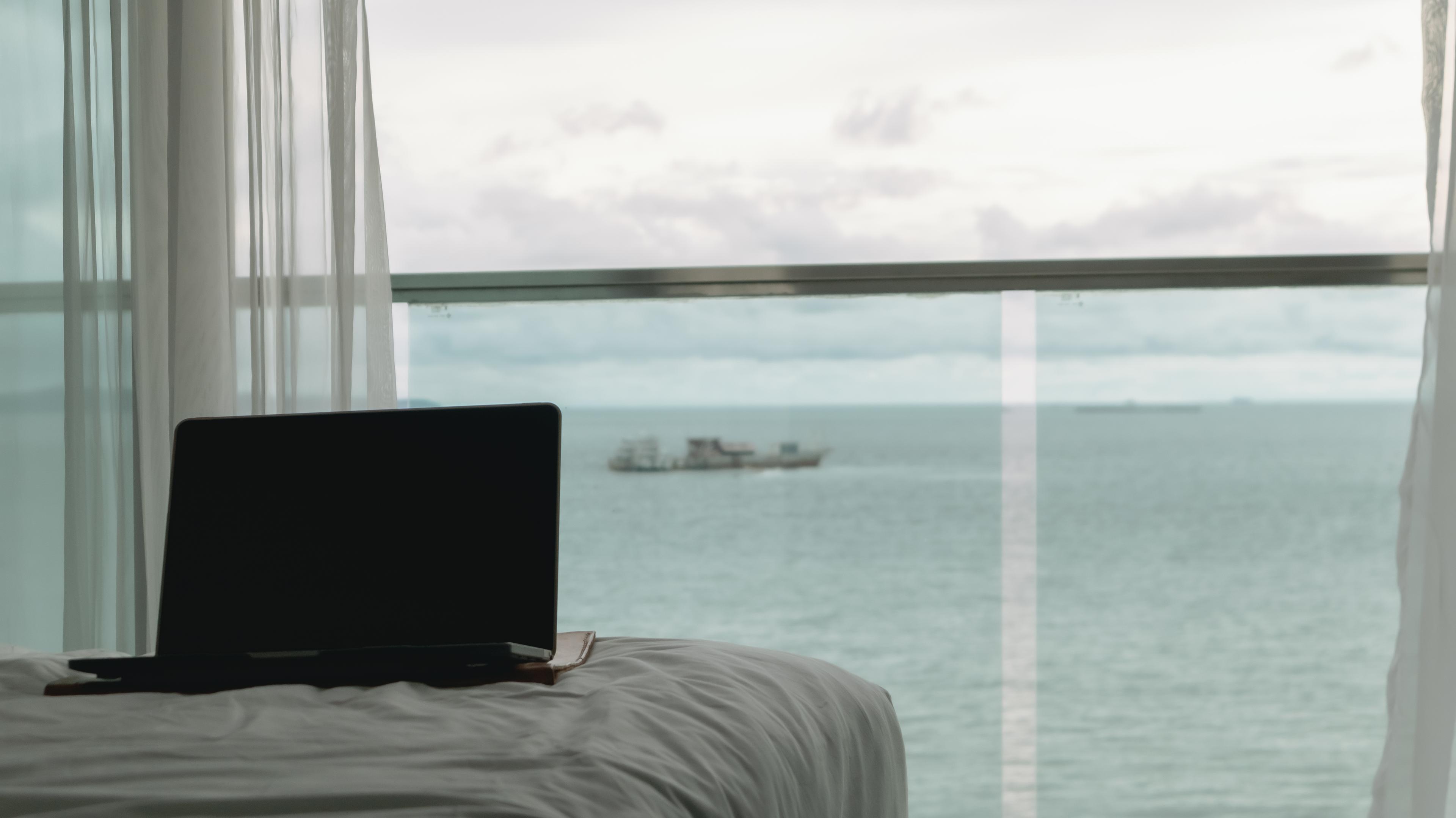 Empty screen laptop on bed with ocean view balcony