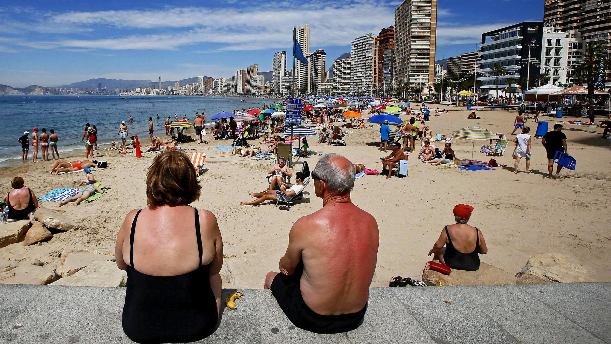 Urlauber sitzen an einem Strand voller Menschen.