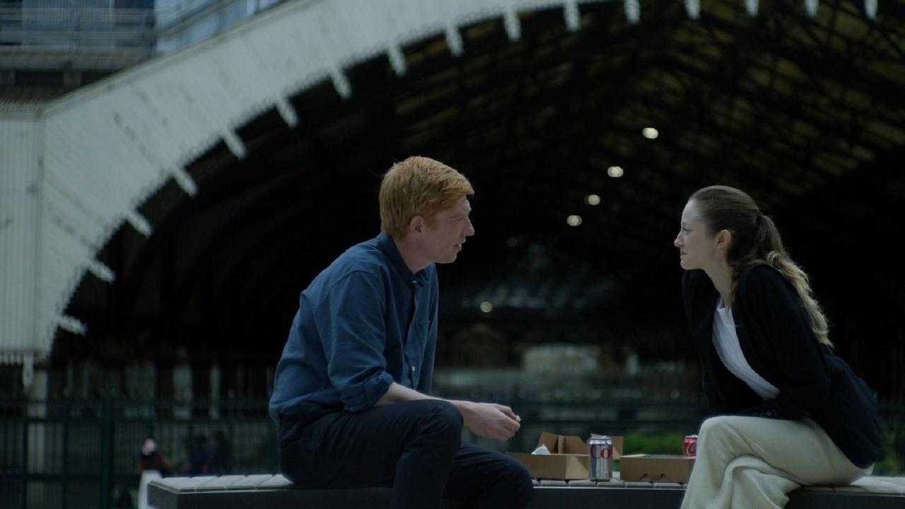 Jack (Domhnall Gleeson) und Alice (Andrea Riseborough) sitzen sich auf einer Bank im Freien gegenüber und unterhalten sich. Zwischen ihnen befinden sich offene Imbissschachteln und Getränkedosen, im Hintergrund wölbt sich eine große Stahlkonstruktion.