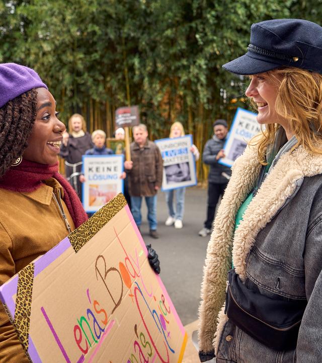 Nikita (Karmela Shako) und Lena (Anna Schimrigk) stehen sich im Freien gegenüber und strahlen sich gegenseitig an. Nikita hält ein Schild in der Hand mit der Aufschrift: "Lena's Body, Lena's Choice". Im Hintergrund sind Demonstranten mit Plakaten.