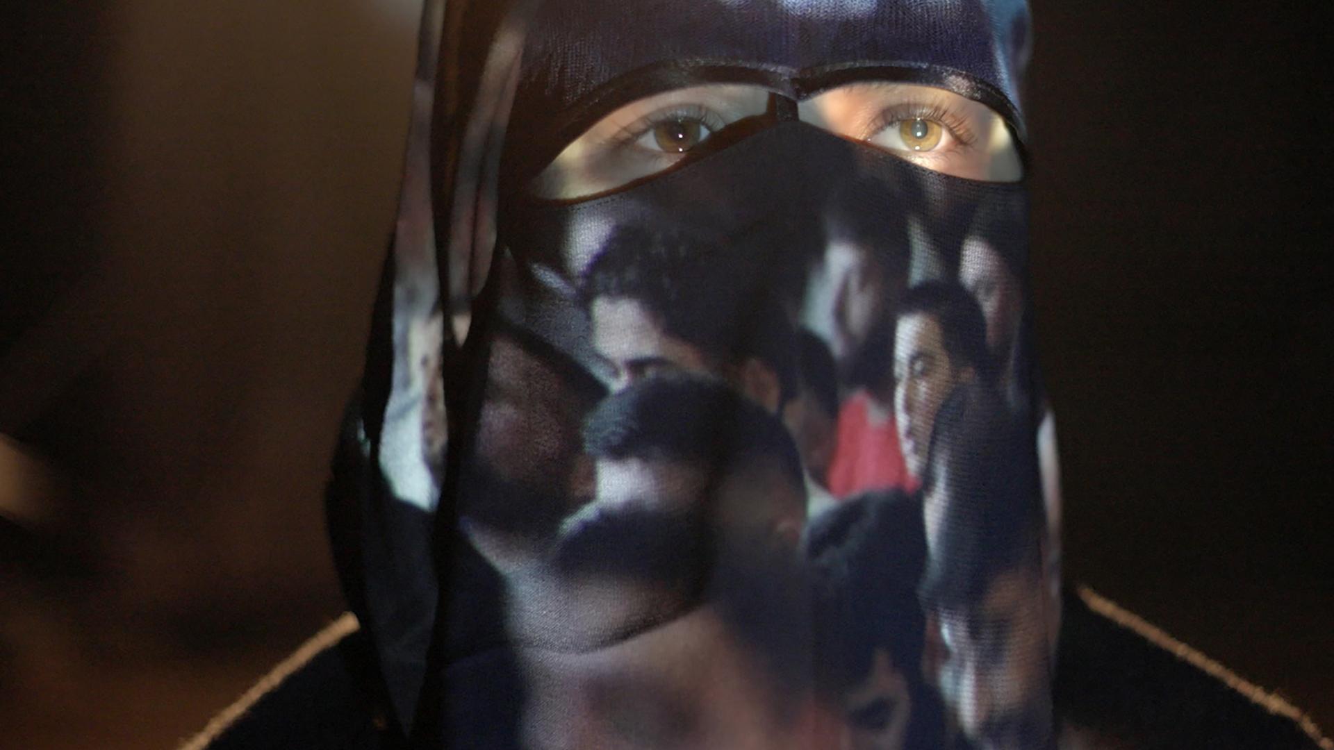 Eine Frau mit Burka, auf der Bilder von Männern projiziert werden.