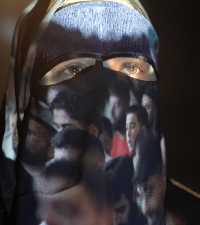 Eine Frau mit Burka, auf der Bilder von Männern projiziert werden.