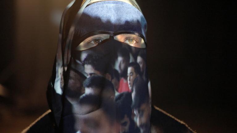 Eine Frau mit Burka, auf der Bilder von Männern projiziert werden.